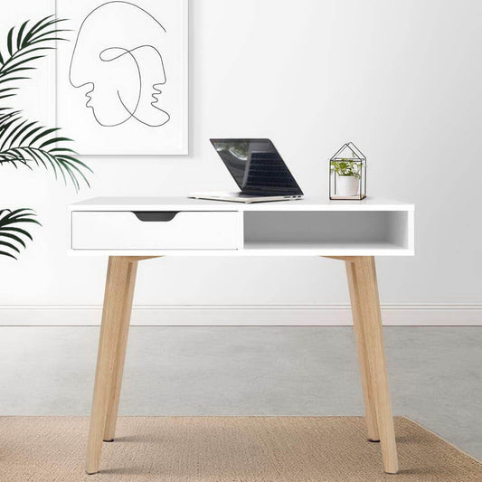 White desk with wooden legs with laptop computer and artwork on wall